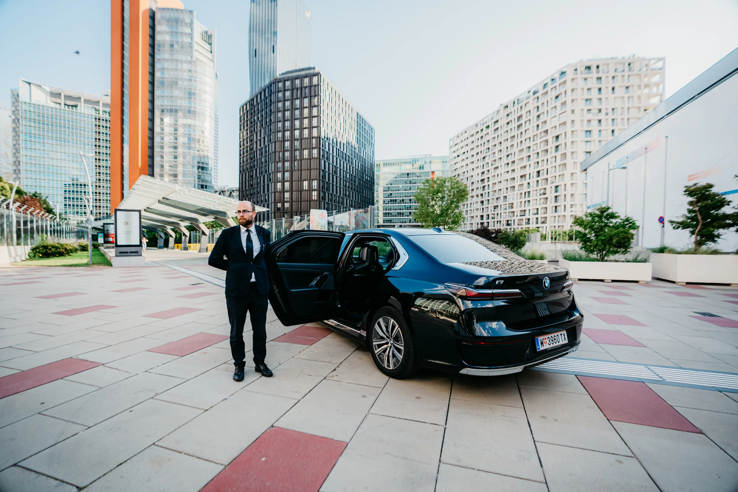 Chauffeur neben dem BMW i7 vor der Wiener Donaustadt-Skyline